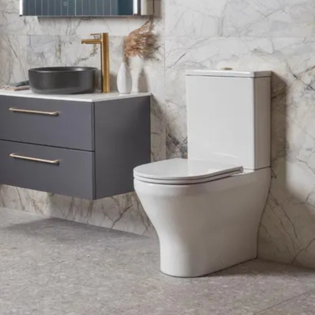 Lifestyle image of the Tavistock Micra Evo Close Coupled Back to Wall Comfort Height Toilet installed against a tiles wall, next to a wall-mounted vanity unit & black freestanding basin